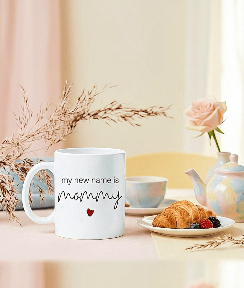 Taza blanca de ceramica con la frase en inglés "Loading mommy box" sobre un mantel en colores pastel junto a accesorios y articulos de desayuno.