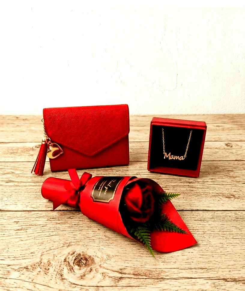 Monedero rojo, colgante dorado con la palabra Mamá y una Rosa Eterna roja sobre superficie de madera clara rustica. 