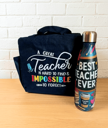 Primer plano de una bolsa termica azul marino con un diseño frontal de frase de agradecimiento para profes en ingles con varios tipos de tipografía en blanco y multicolor, a su lado puede verse una botella termo con interior en Acero inoxidable y porcel exterior puede leerse "BEST TEACHER EVER" con motivos escolares de colores, lasdos cosas están sobre una superficie de madera clara y pared blanca.