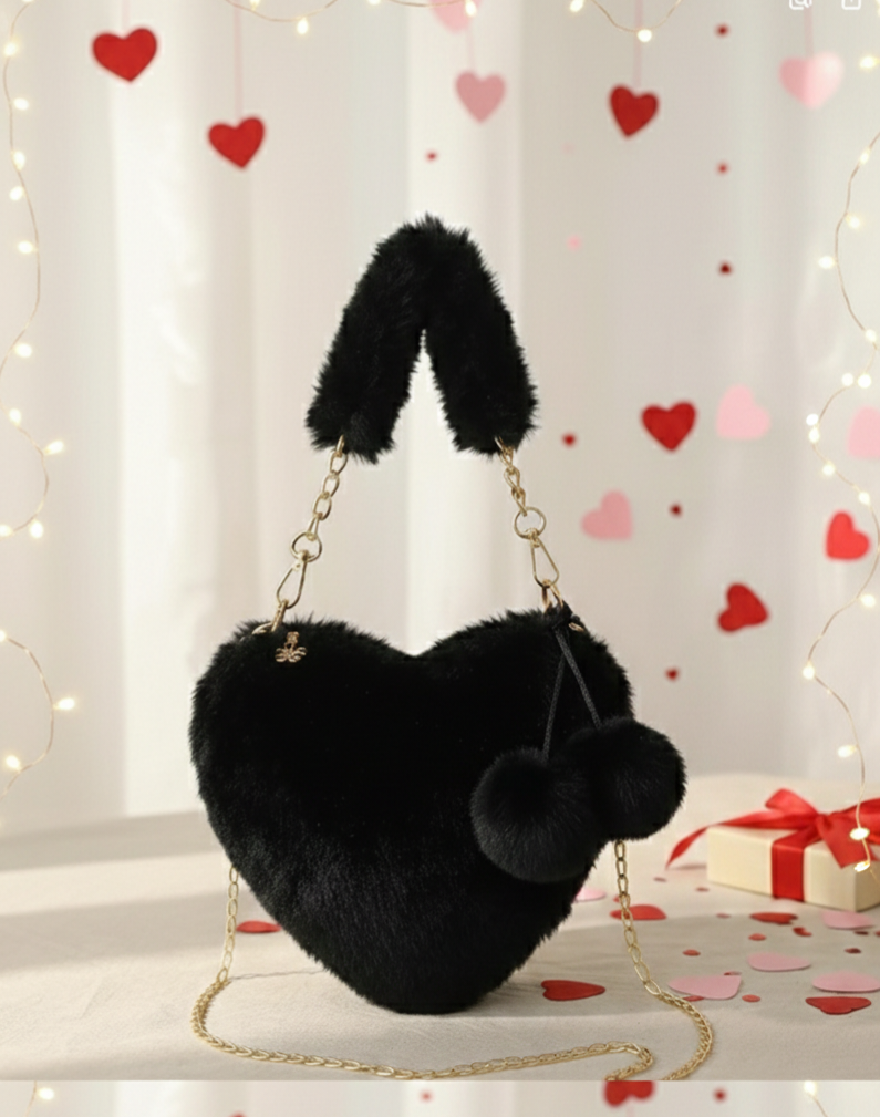 Bolso de mano negro, con textura de peluche en forma de corazón,  detalles en dorado y pompones decorativos.