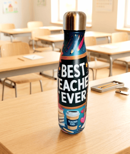 Primer plano de una Botella Termo con interior de Acero inoxidable y un exteror con la frase: "Best Teacher Ever" con tipografia clasica de color blanco y diseño colorido de motivos escolares sobre una superficie de madera clara y un fondo de mesas y sillas de aula escolar.