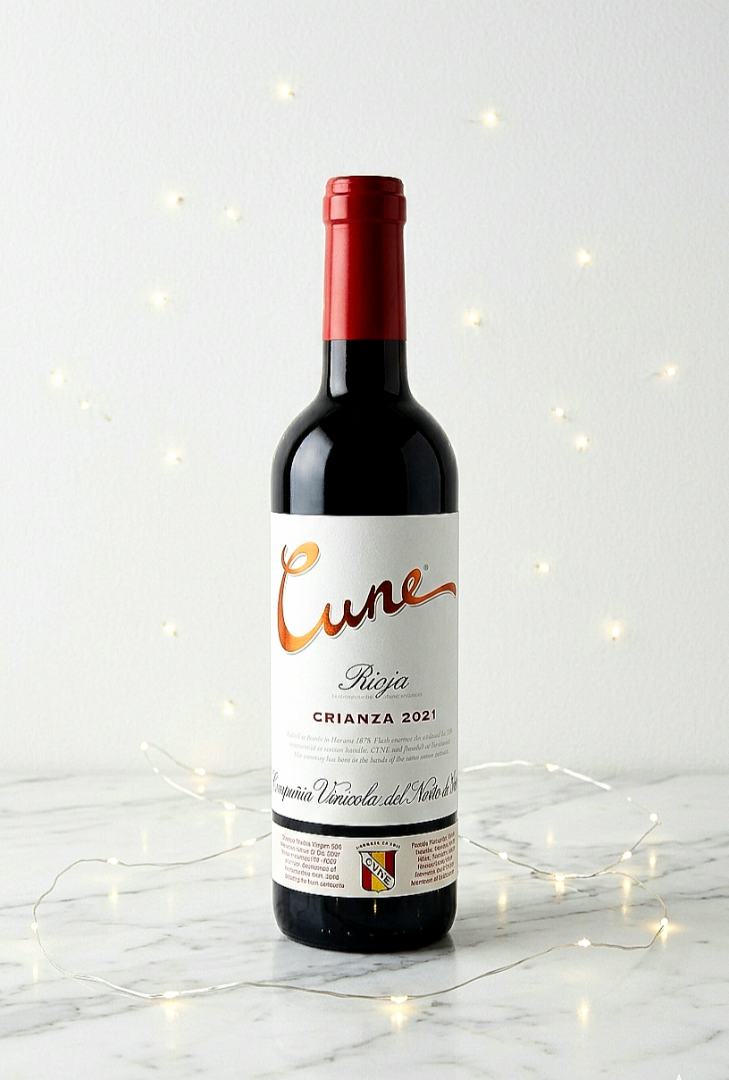 Una botella de vino tinto Cune Rioja Crianza 2021 sobre mesa de marmol blanca con luces led decorativas .