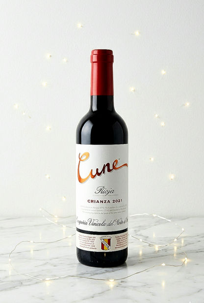 Una botella de vino tinto Cune Rioja Crianza 2021 sobre mesa de marmol blanca con luces led decorativas .