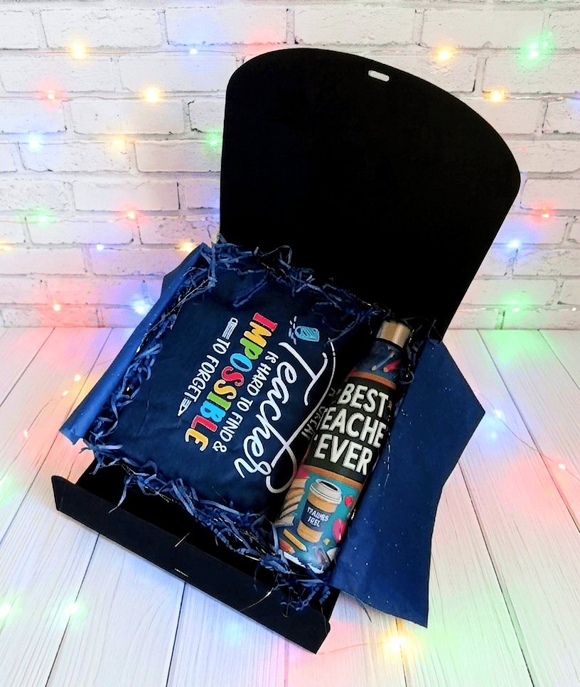 Caja de regalo abierta vista desde arriba, mostrando una bolsa termica plegada con un texto de agradecimiento en inglés, con dos tipos de tipografia: Una tipografia moderna en color blanco y otra tipografia mas clásica y con letras de colores, a su lado hay una botella termica con interior de acero inoxidable y se puede leer la frase "Best Teacher Ever" con ilustraciones y motivos escolares. La caja se encuentra sobre una superficie de tarima de madera blanca con luces led de colores.