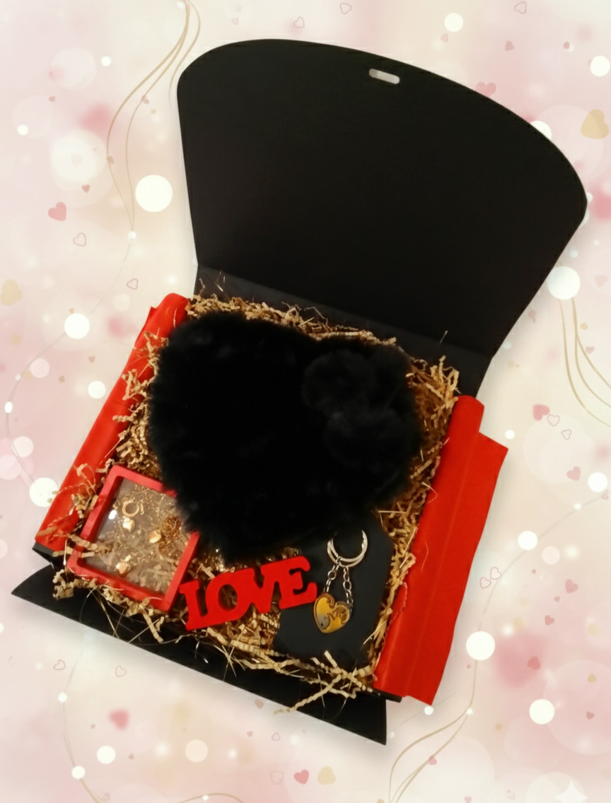 Caja negra elegante abierta con bolso negro de peluche, conjunto de joyeria dorada y llaveros de gatos para pareja sobre virutas de papel.