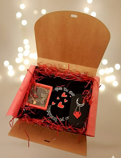 Caja de regalo abierta con virutas de papel rojo que contiene un neceser negro, un  llavero de corazon y un set de joyeria en caja transparente.