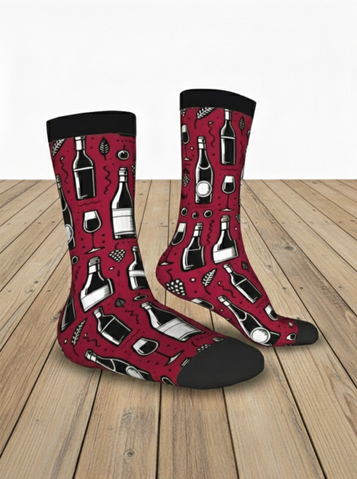 Par de calcetines color rojo borgoña con estampado de botellas de vino, copas y uvas con talon y punta negra sobre suelo de madera clara.
