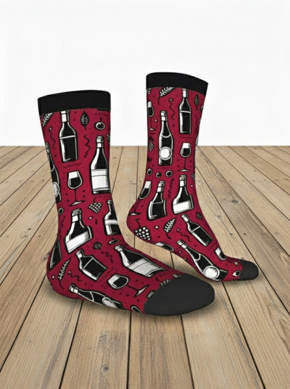 Par de calcetines color rojo borgoña con estampado de botellas de vino, copas y uvas con talon y punta negra sobre suelo de madera clara.