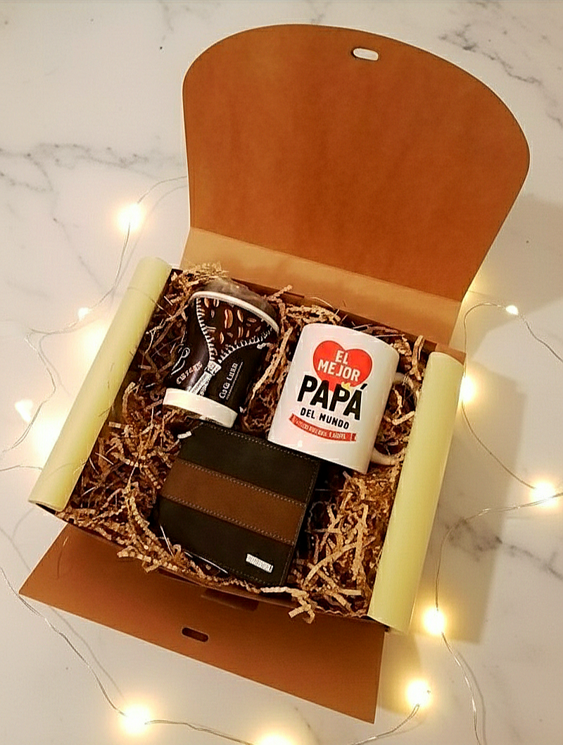 Caja de regalo abierta mostrando una taza de dia del padre, una cartera de cuero sintetico con raya horizontal, un envase de Caffee latte que contiene calcetines sobre un fondo de marmol blanco con luces led.