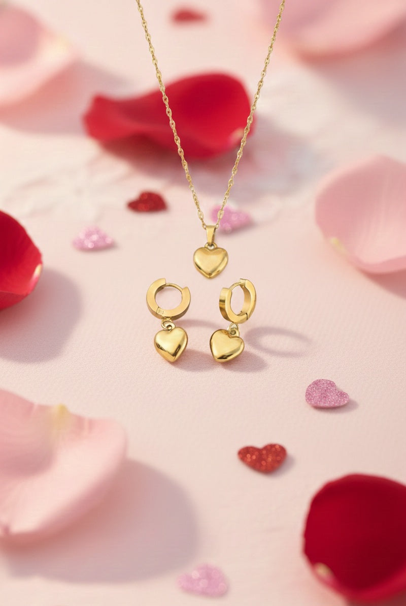 Set de colgante y pendientes, piezas doradas en Acero en forma de corazón sobre un fondo rosa con pétalos.