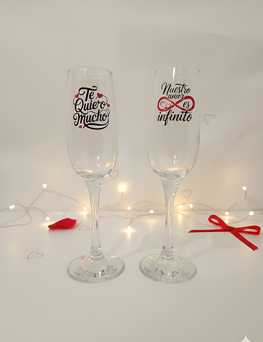 Pareja de copas de cava personalizadas con frases romanticas de San Valentin sobre fondo con luces led  y detalles rojos.