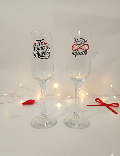 Pareja de copas de cava personalizadas con frases romanticas de San Valentin sobre fondo con luces led  y detalles rojos.