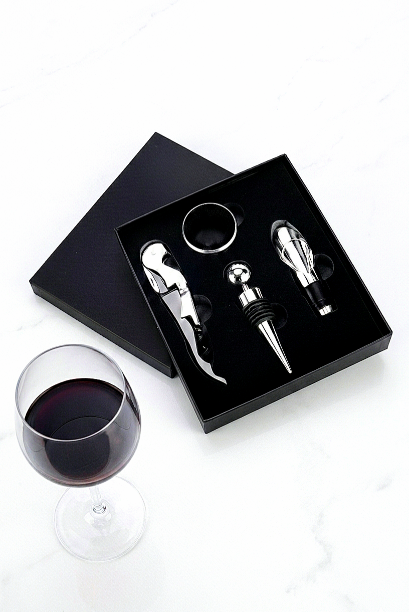 Estuche negro de regalo premium abierto que muestra un kit de 4 accesorios de vino plateados: Sacacorchos, tapón de botella,  aireador y anillo antigoteo.