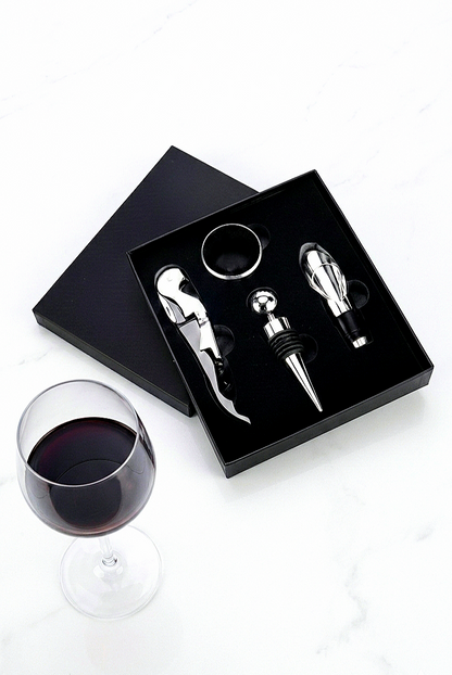 Estuche negro de regalo premium abierto que muestra un kit de 4 accesorios de vino plateados: Sacacorchos, tapón de botella,  aireador y anillo antigoteo.