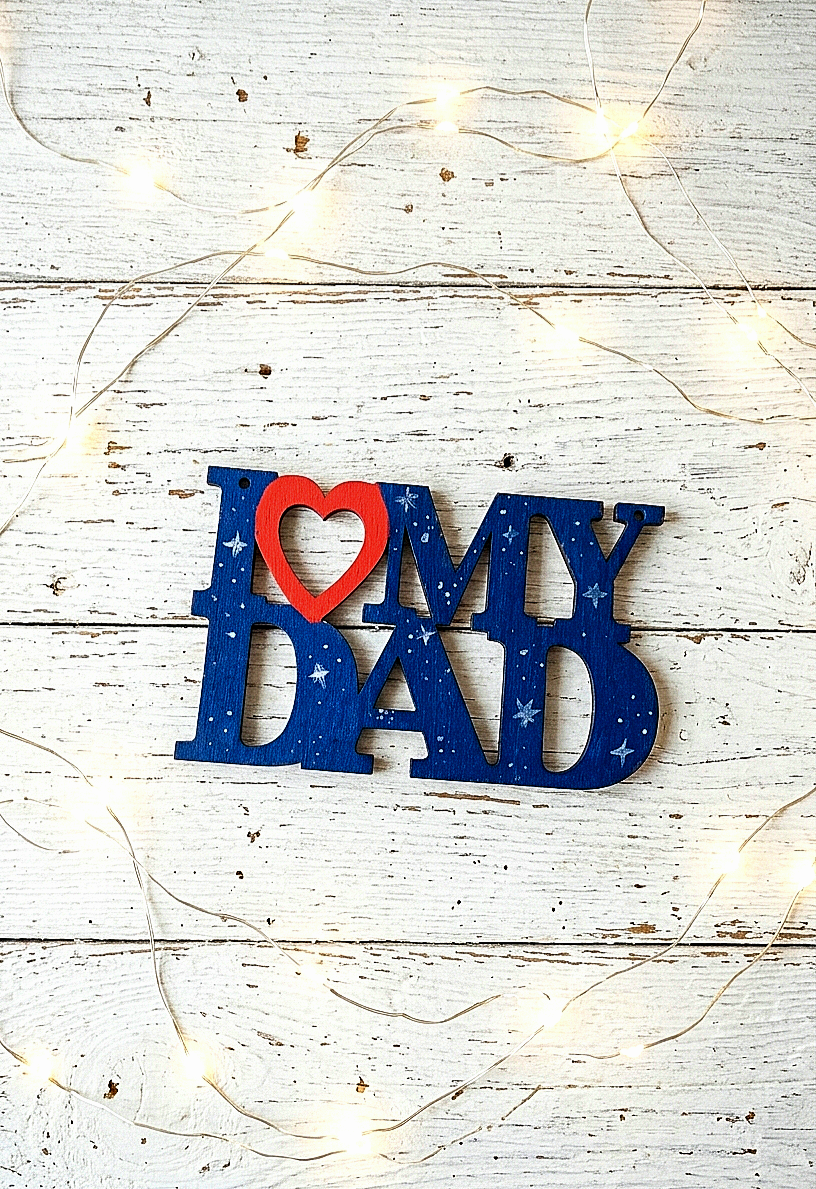 Letrero de madera "I ❤️ My Dad" con los colores y diseño caracteristicos de la Nasa en color azul cobalto con estrellas blacas y corazon rojo sobre fondo de madera blanca y luces led.