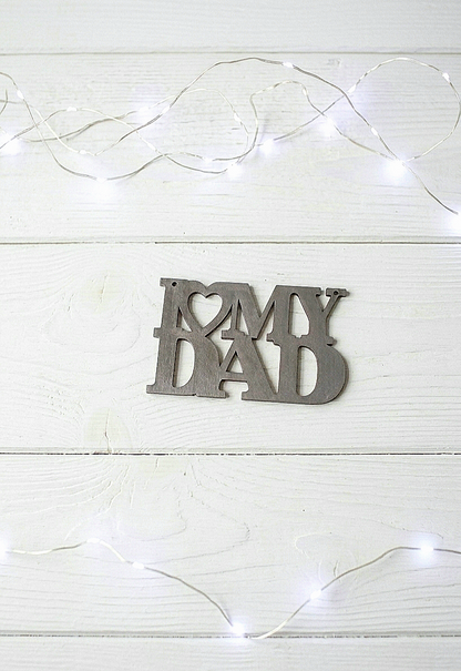Letrero de madera en color gris metalizado "I love my dad" sobre fondo de madera blanco con luces led.