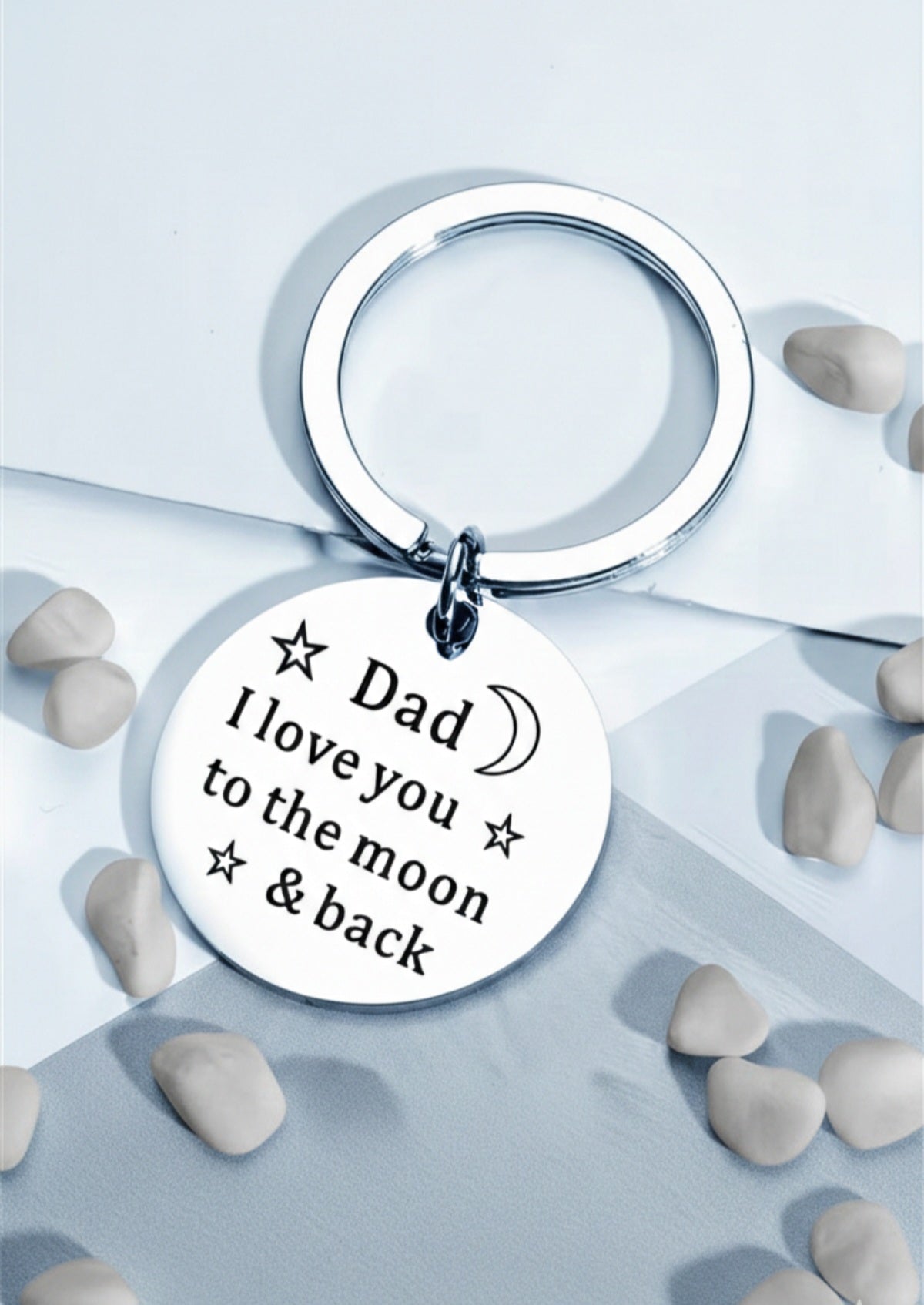 Llavero circular de acero plateado con la frase grabada " Dad I love you the moon & back" sobre fondo azul con pequeñas piedras blancas