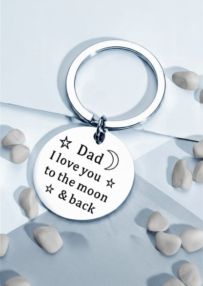 Llavero circular de acero plateado con la frase grabada " Dad I love you the moon & back" sobre fondo azul con pequeñas piedras blancas