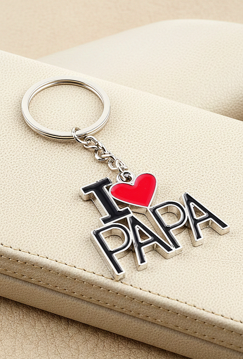 Primer plano de un llavero metalico con el texto I Love Papá con un corazon rojo brillante sobre un fondo de cuero color beige.