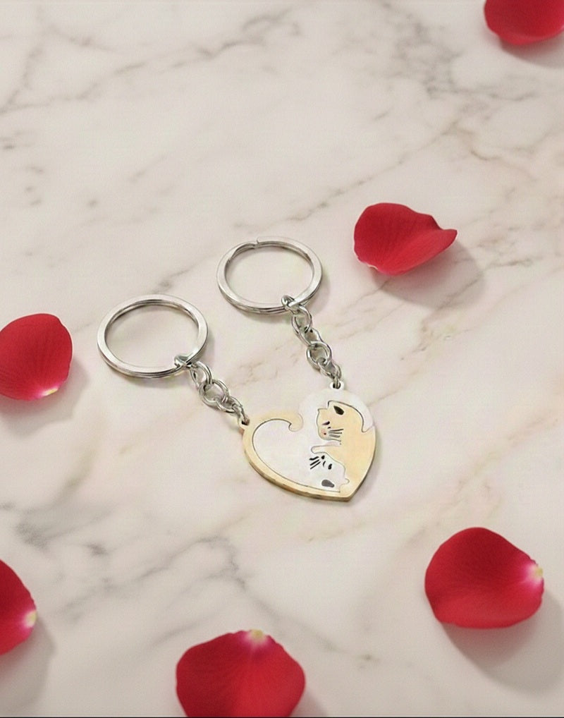 Llaveros para parejas, dos gatos que se unen formando un corazon sobre fondo blanco con petalos rojos.
