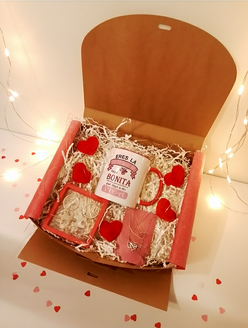 Caja de regalo LOVE LUCK BOX que incluye taza con frase "Eres la casualidad más bonita que llegó a mi vida" colgante de corazon y simbolo infinito entrelazados, llaveros de puzzle y corazones rojos con decoración de virutas de papel.