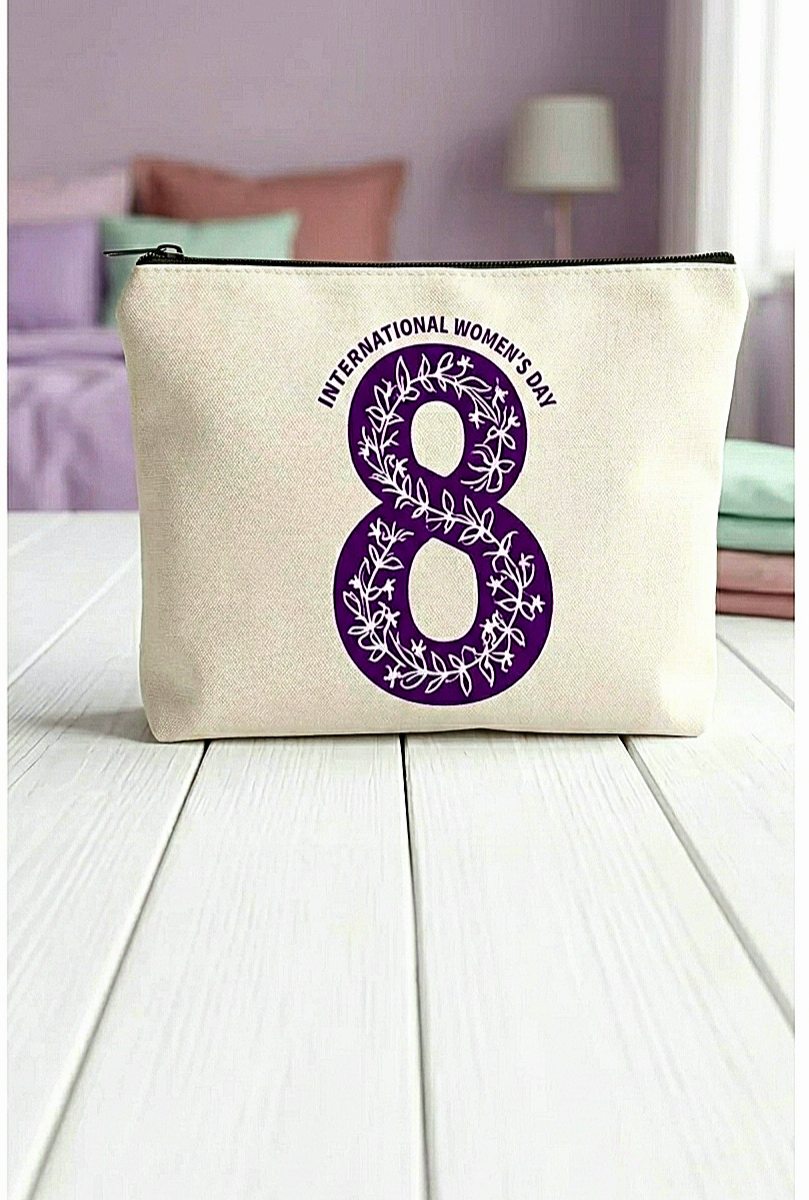 Neceser con el numero 8 en color morado con diseño de flores entrelazadas en su interior y con la frase " International women's day" en la parte superior del 8 formando un semicírculo, sobre superficie blanca y fondo de dormitorio en colores pastel.