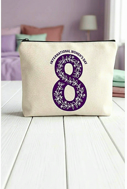 Neceser con el numero 8 en color morado con diseño de flores entrelazadas en su interior y con la frase " International women's day" en la parte superior del 8 formando un semicírculo, sobre superficie blanca y fondo de dormitorio en colores pastel.