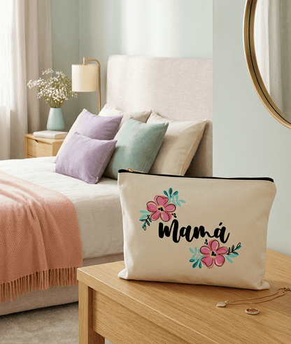 Neceser de lona con la palabra "Mama" y dos flores de loto, en messita de noche de madera clara, al fondo se ve una cama con cojines en colores pastel, una lámpara y un espejo circular en la pared.