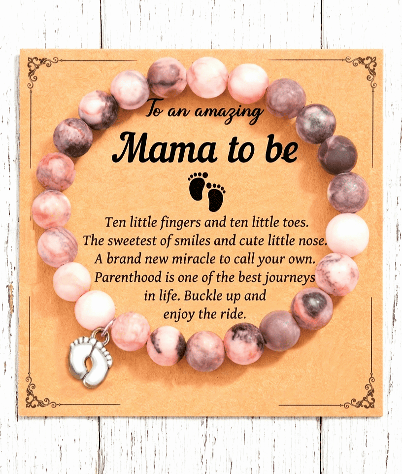 Primer plano de una pulsera de cuentas en color pastel con dije de pies de bebé en color plateado sobre una tarjeta de papel kraft con un texto emotivo en inglés para fururas mamas. 