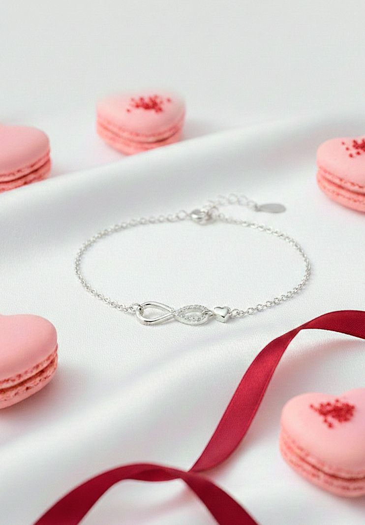 Pulsera de plata con simbolo de Infinito y pequeño corazón sobre fondo de seda blanca.