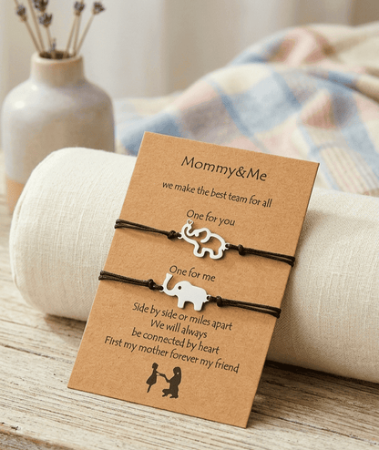 Primer plano detallado de una tarjeta kraft apoyada sobre un cilindro de tela de lino. La tarjeta contiene un texto en inglés con una ilustración. Sujetas a la tarjeta hay dos pulseras de cuerda negra ajustables con pequeños dijes de elefantes plateados. El dije superior es la silueta de un elefante y el inferior un elefante solido.