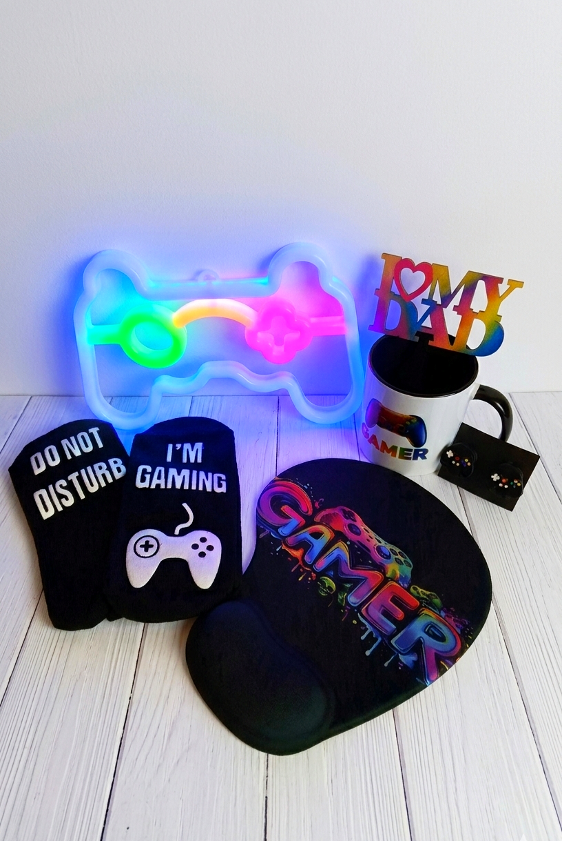 Conjunto de regalos Gamer compuesto por lampara de neón, taza de ceramica, mousepad, calcetines y protectores de cable sobre fondo de madera blanca 