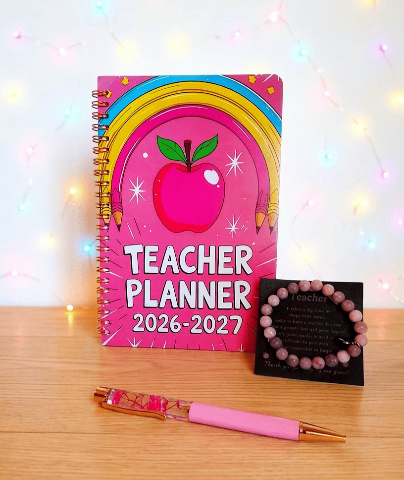 Conjunto de regalos para profesora sobre una superficie de madera clara y pared blanca con luces led, formado por una agenda planificadora de color fucsia con diseño Retro-Pop, a su lado se encuentra una pulsera de cuentas en tonos rosados presentada en tarjeta negra con dedicatoria de letras en dorado, por ultimo en el centro se puede ver un boligrafo de color rosa en la parte inferior y acrilico con flores fucsias en la parte superior.