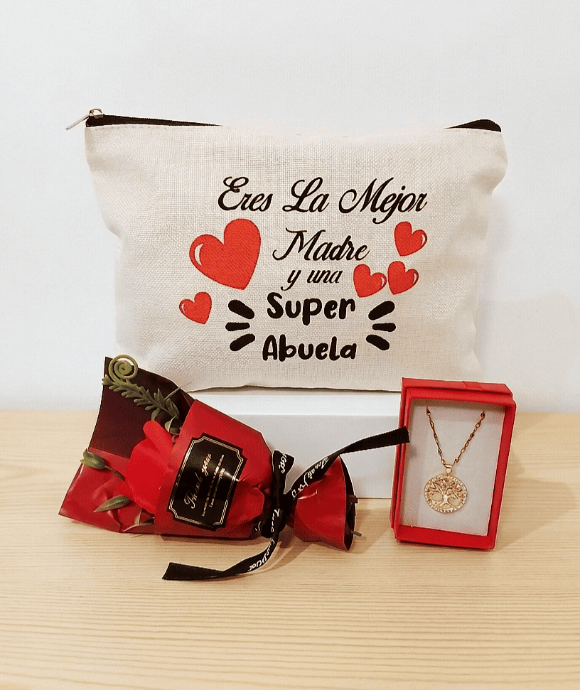 Set de regalos compuesto por un neceser de lino blanco con la frase " Eres la mejor madre y una Super abuela" un colgante de arbol de la vida en Acero dorado y una rosa con envoltorio rojo, todo sobre una superficie de madera clara. 