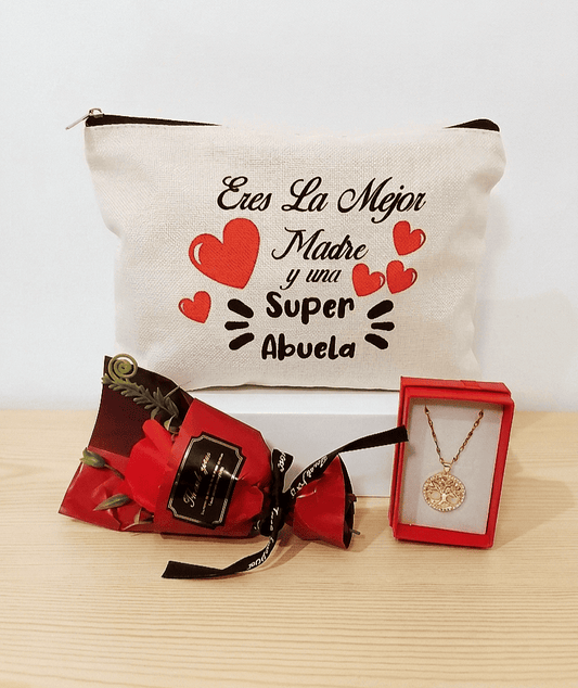Set de regalos compuesto por un neceser de lino blanco con la frase " Eres la mejor madre y una Super abuela" un colgante de arbol de la vida en Acero dorado y una rosa con envoltorio rojo, todo sobre una superficie de madera clara. 