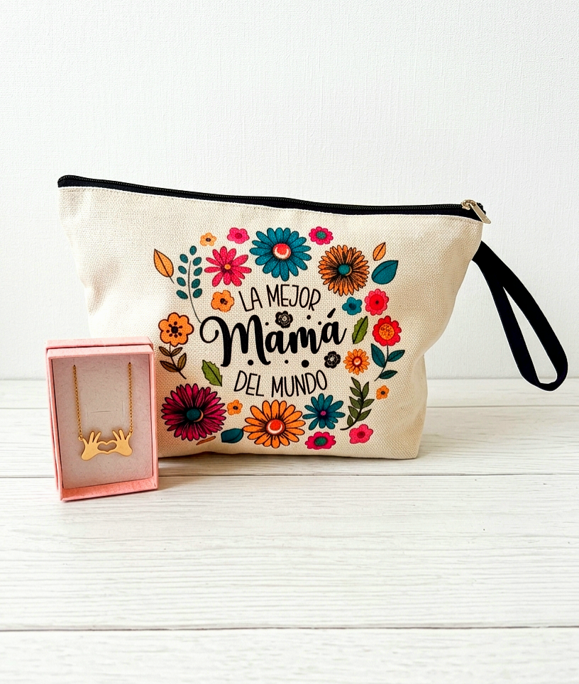 Neceser con diseño de estampado floral con la frase "La mejor madre del mundo" junto a una caja rosa que contiene un colgante dorado en Acero inoxidable de dos manos formando un corazón sobre una superficie de madera blanca. 